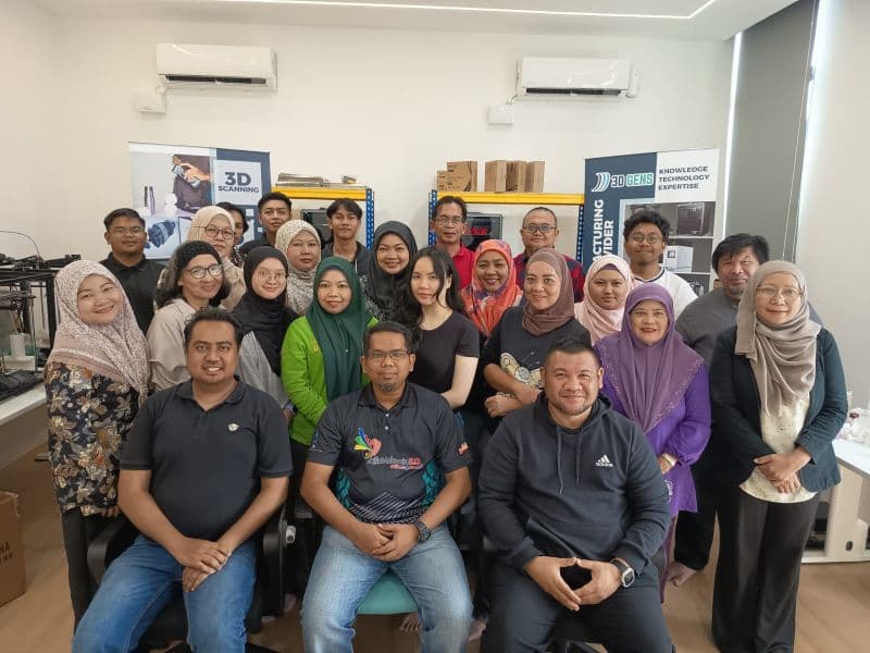 Group photo of 3D Gens trainers and participants inside the 3D Gens facility with 3D scanning equipment and banner visible in the background