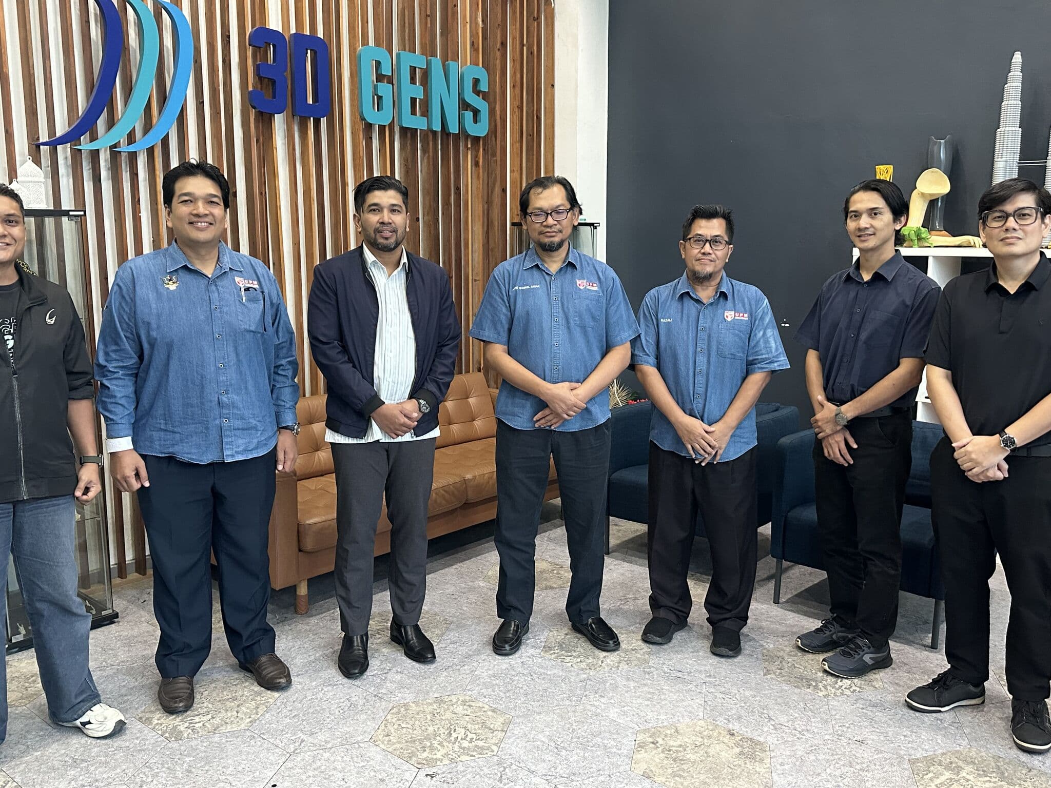 UPM research team and 3D Gens team posing together in front of the 3D Gens reception, with 3D-printed artefacts displayed in the background